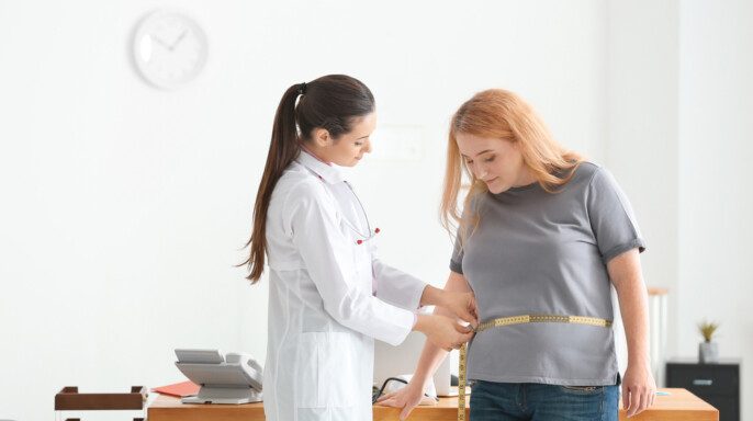 Doctora joven midiendo cintura de mujer con sobrepeso con centímetro en clínica — Foto de Stock Doctora joven midiendo cintura de mujer con sobrepeso con centímetro en consultorio.