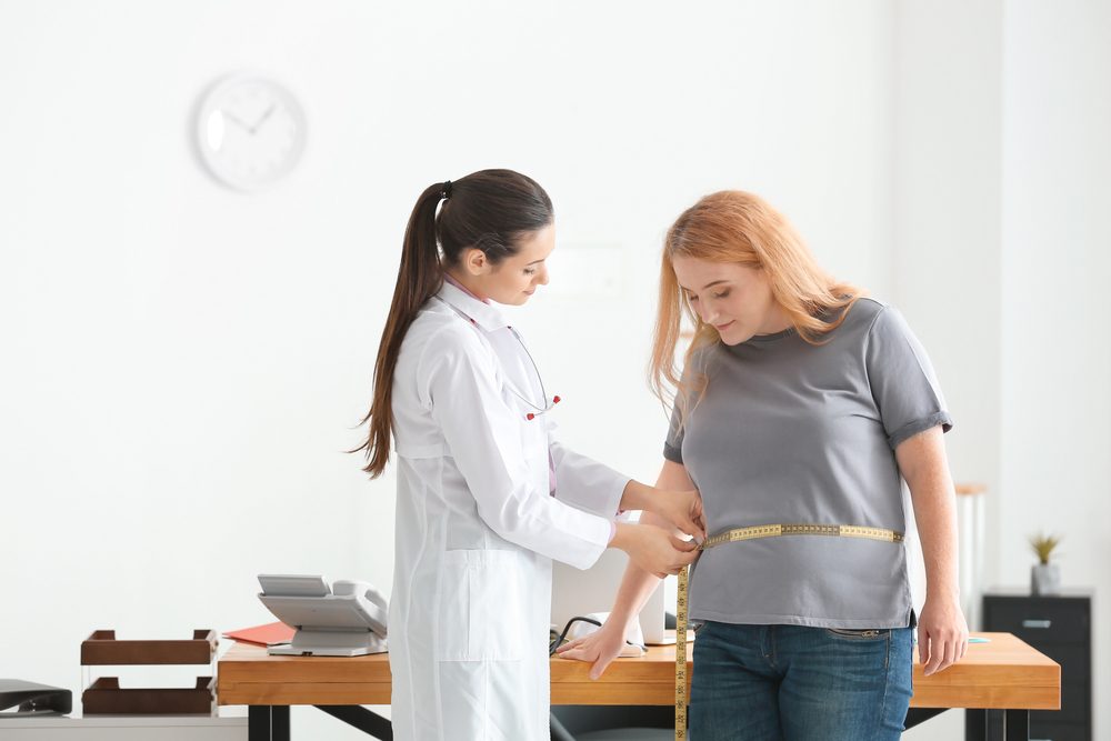 Doctora joven midiendo cintura de mujer con sobrepeso con centímetro en clínica — Foto de Stock Doctora joven midiendo cintura de mujer con sobrepeso con centímetro en consultorio.