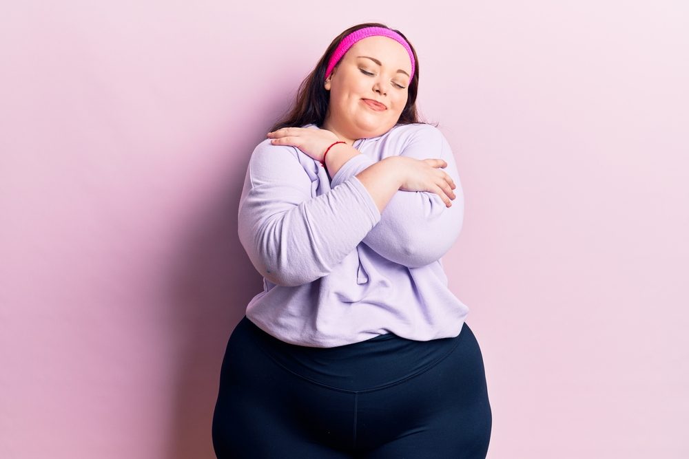 Joven mujer de talla grande con ropa deportiva abrazándose feliz