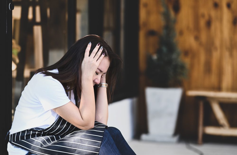 Joven en una cafetería sintiendo estrés o depresión mientras se toca la cabeza