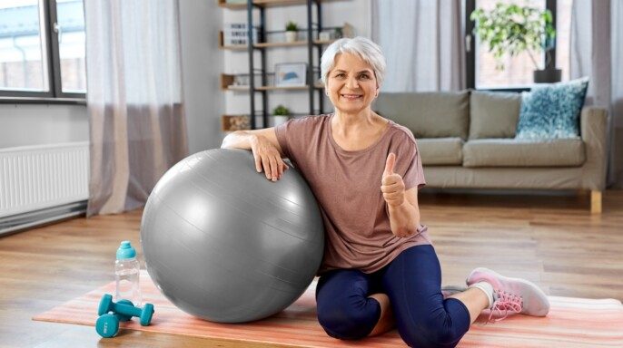 adulta mujer mayor sonrie con bola de ejercicio en casa