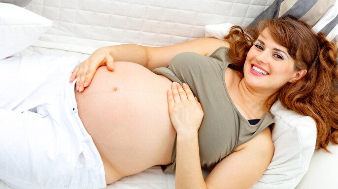 Sonriendo hermosa mujer embarazada relajándose en el sofá y sosteniendo su vientre . — Foto de Stock Sonriendo hermosa mujer embarazada relajándose en el sofá.