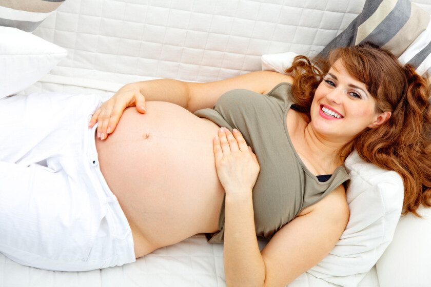 Sonriendo hermosa mujer embarazada relajándose en el sofá y sosteniendo su vientre . — Foto de Stock Sonriendo hermosa mujer embarazada relajándose en el sofá.