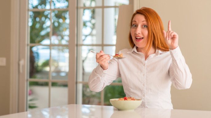 Mujer Pelirroja Comiendo Cereales Con Frambuesas Casa Sorprendida Con Una — Foto de Stock Mujer pelirroja comiendo cereales con frambuesas en casa sorprendida.