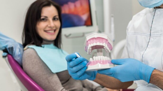 dentisa sostiene modelo de diente paciente observa con una sonrisa