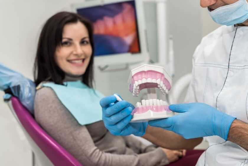 dentisa sostiene modelo de diente paciente observa con una sonrisa