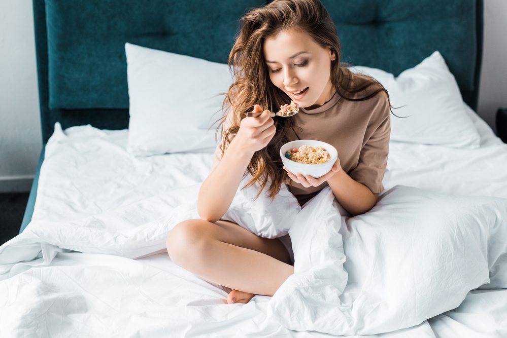 Chica comiendo avena para el desayuno mientras está sentado en la cama.