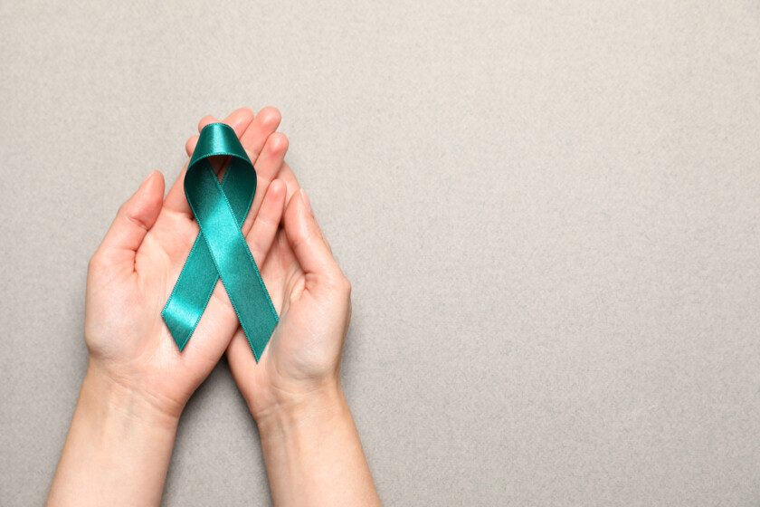 Mujer sosteniendo cinta de conciencia verde azulado sobre cáncer cervicouterino
