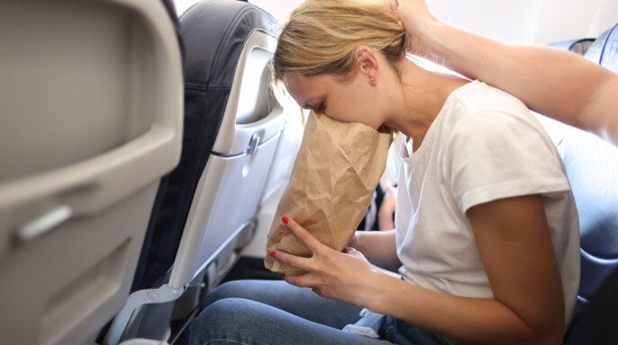 Mujer joven vomitando en bolsa de papel en cabina de avión — Foto de Stock New Borrar fondo Guardar Compartir Muestra Mujer joven vomitando en bolsa de papel en cabina de avión