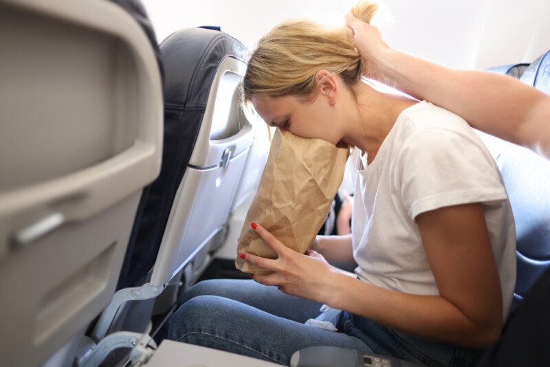 Mujer joven vomitando en bolsa de papel en cabina de avión — Foto de Stock New Borrar fondo Guardar Compartir Muestra Mujer joven vomitando en bolsa de papel en cabina de avión