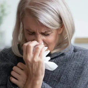 Ill mature woman covered with blanket blowing running nose sneeze in tissue suffer from allergy flu, allergic old lady hold handkerchief got hay fever rhinitis symptom cough at home, allergy concept