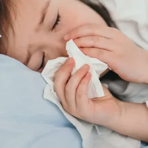 The little girl caught a cold. Children sneeze into a handkerchief. The child is ill and is being treated at home. Seasonal colds in children.